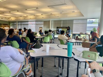 adults sitting at tables with female presenter talking with powerpoint