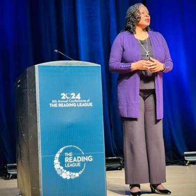 Woman standing with podium that says reading league under spotlight