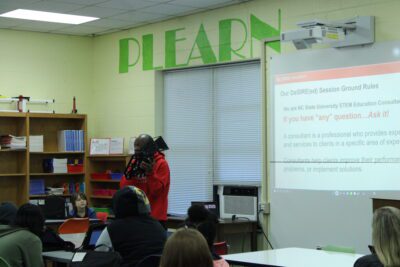 man in red hoodie holding robotic part in front of projector