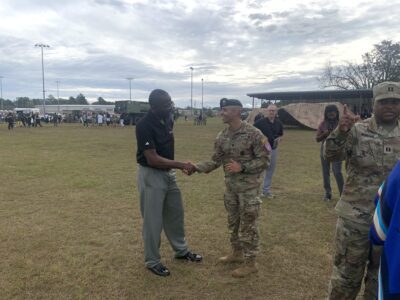 robert taylor in a black polo shaking hands with Ramon Ramos who is in his camouflage uniform