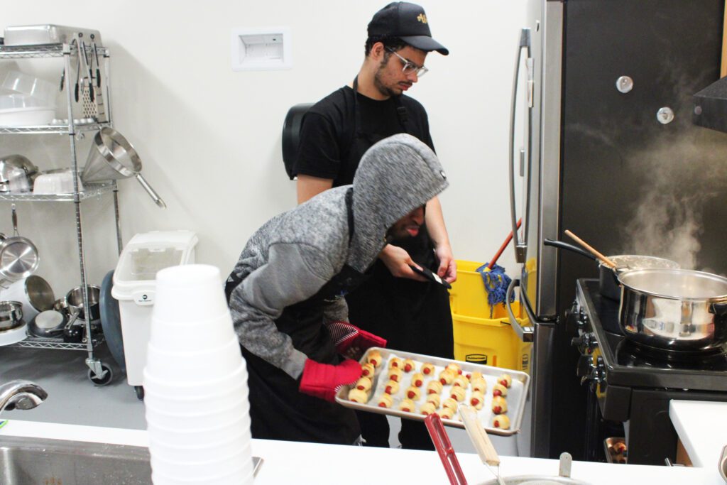 student taking pigs in a blanket rolls out of the oven with pots on the stove