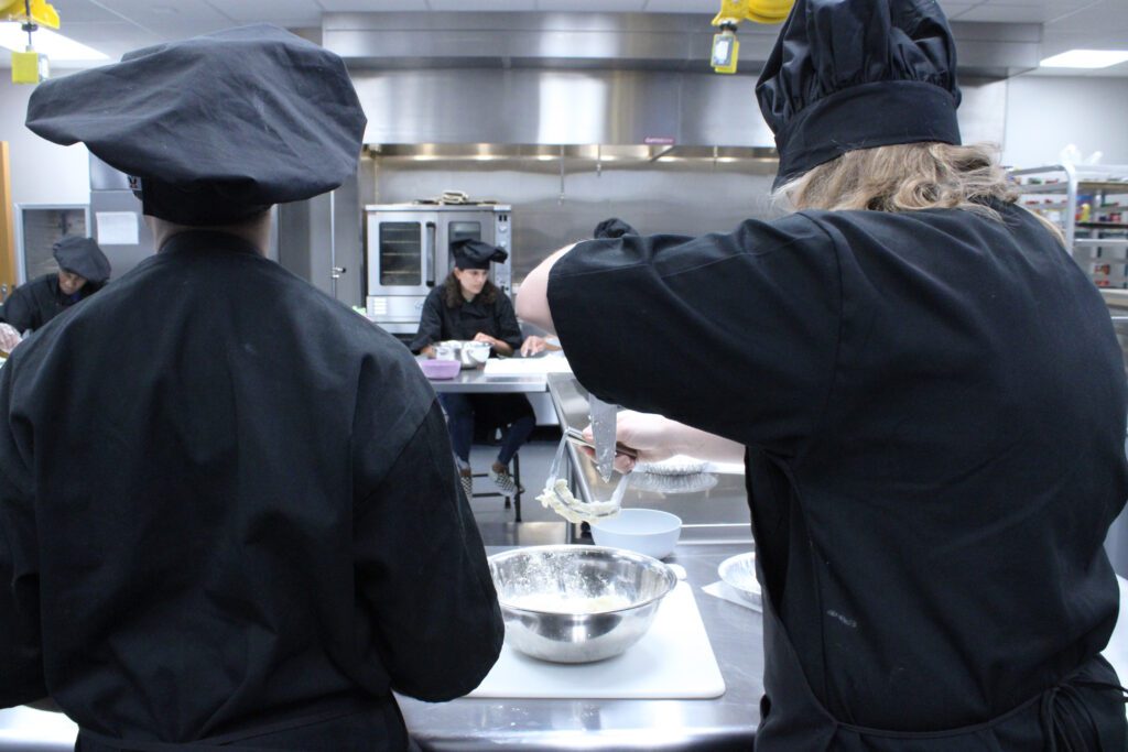 students in black chef outfits getting batter off of a blade