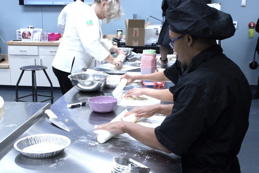 students rolling out dough on a steel counter for a pie