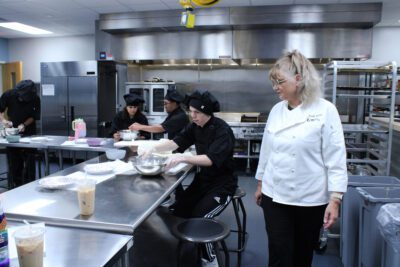 A culinary instructor watching her student stir batter